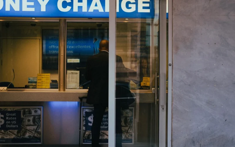 A customer at a currency exchange office window with rates displayed