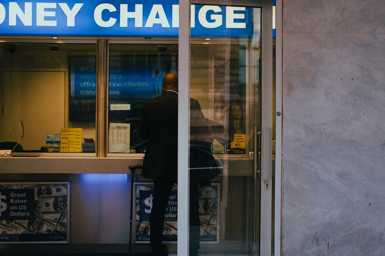 A customer at a currency exchange office window with rates displayed