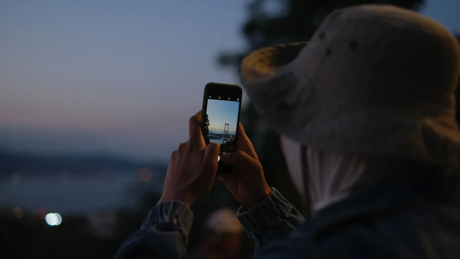 A visitor photographing the Bosphorus Bridge in Istanbul on a smartphone at dusk