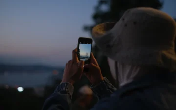 A visitor photographing the Bosphorus Bridge in Istanbul on a smartphone at dusk