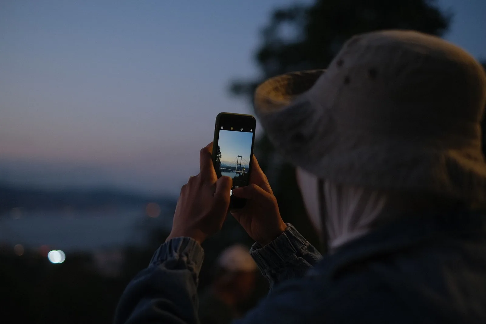 A visitor photographing the Bosphorus Bridge in Istanbul on a smartphone at dusk